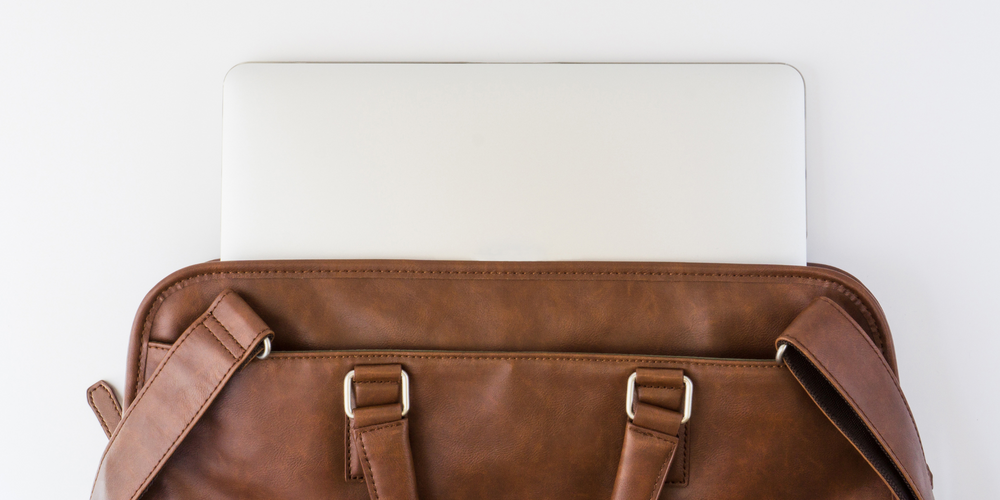 Nahaufnahme einer braunen Laptoptasche, weißer Laptop ragt oben heraus, minimalistischer Hintergrund