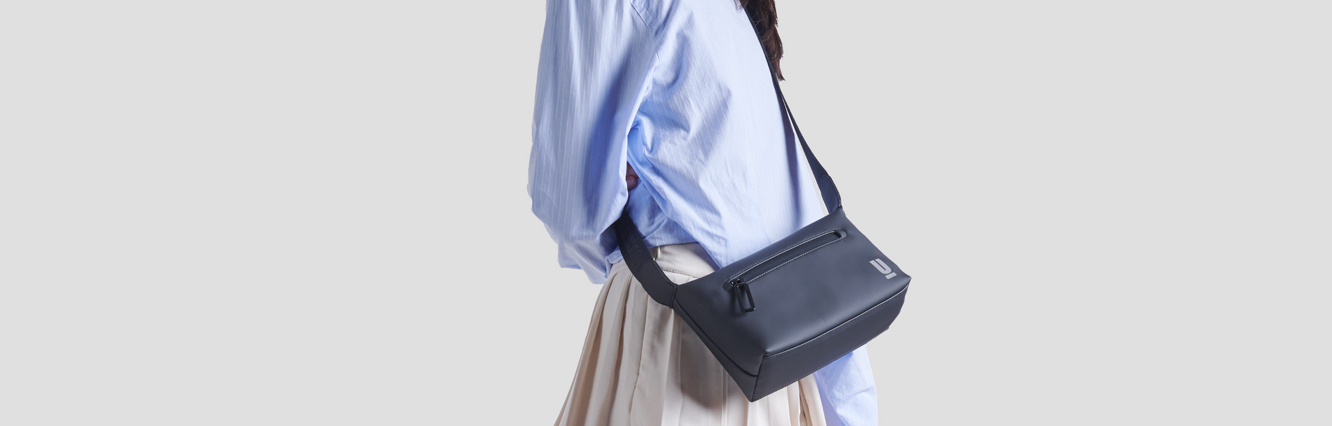 The Urban Society, Umhängetasche, schwarz, minimalistisch, Person mit blauer Hemdbluse, helle Kleidung, stilvoll, urban, clean, modern